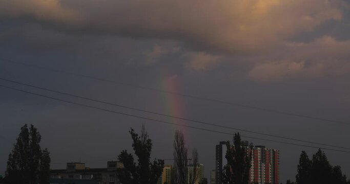 Beautiful rainbow over city houses after rain. Cloudy sky in the background.