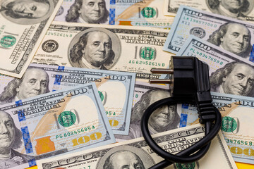 Plug from an electric cord tied in a knot on a blurred background of dollars, selective focus