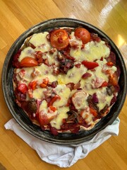 Close up of home made freshly baked hot vegetarian pizza lunch with sour dough bread base, mushroom, tomato, onion, pepper, courgette, cheese topping with basil herbs on wood kitchen surface flat lay