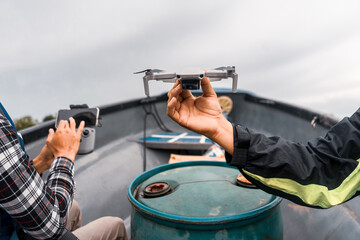 Two unrecognizable Latino men riding a boat and setting up a drone in El Rama, Nicaragua