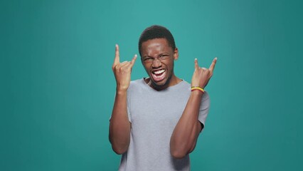 Funky cool man showing rock metal sign with hands in front of camera, expressing fun punk music with positive energy. Male hipster rocker gesturing devil horns symbol for entertainment.