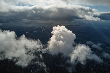 Aerial view from airplane window at high altitude of distant city covered with white puffy cumulus...