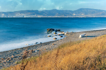 A long exposure shot of a sea with yellow foliage in the foreground and mountains in the background.