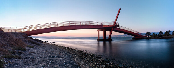A horizontal panoramic shot of a bridge crossing over sea at the sunset. Long exposure.