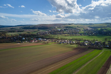 Fototapeta na wymiar Aerial view of plowed agricultural fields with cultivated fertile soil prepared for planting crops between green woods in spring