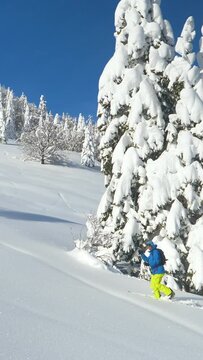 DRONE: Fit Caucasian man observes the beautiful snow covered nature while crossing the wintry landscape during a ski touring trip to Bohinj. Active male tourist hikes along a hill while splitboarding.