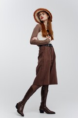 A full-length shot of a red-haired girl in a hat and boots in the studio on a white background....
