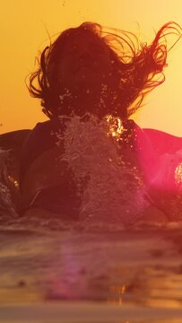 SLOW MOTION, LENS FLARE, CLOSE UP, DOF: Young woman falls into the tranquil ocean water with outstretched arms. Fit female tourist leaps back first and breaks the surface of the calm Adriatic sea.