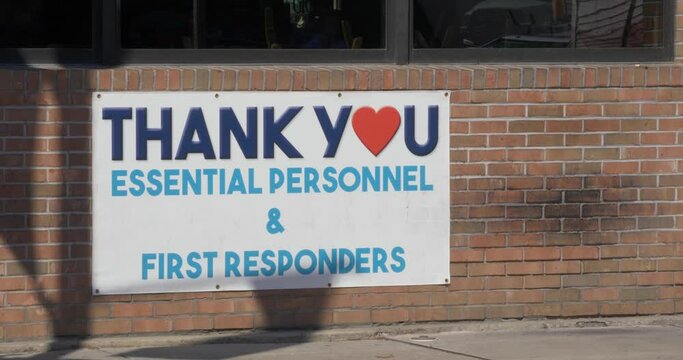 A closeup view of a Thank You Essential Personnel and First Responders banner on a small business along the main street of a small town.  	