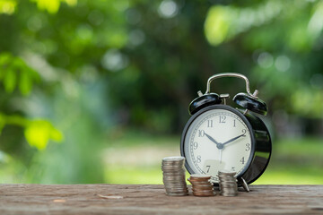 Stack of coins steps up with alarm clock with green nature background, investment
