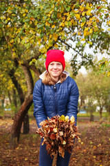 Defocus smiling teen girl holding dry leaves. Child volunteer rakes and grabs a small pile of...