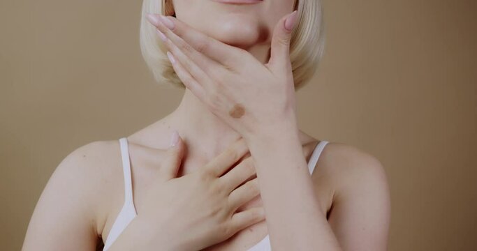 Cropped view of young woman in white lingerie, isolated on natural sandy background, gently touching her neck with both hands.