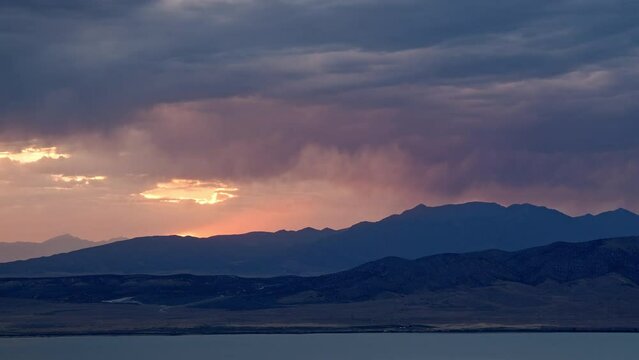 Sunset timelapse as rainstorm moves over the mountains looking past Utah Lake during summer monsoon.
