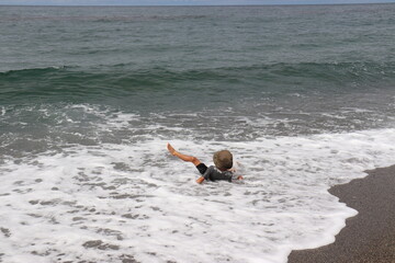 波打ち際で洋服を着たまま転がり遊ぶ男の子