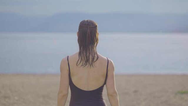 Rear view of an attractive wet girl walking on a public park beach