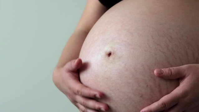 Close up in woman in third trimester of pregnancy rubbing her bare belly