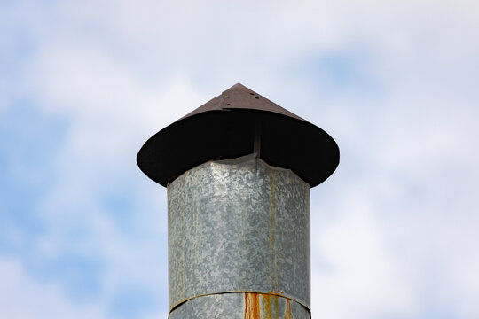 Close up to an old metallic chimney with conic head or cowl against cloudy sky