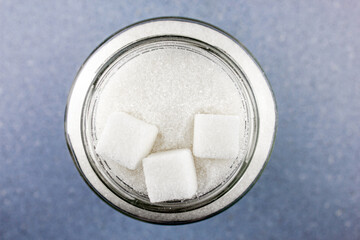 Sugar in a glass jar.Pieces of sugar cubes and sugar crumbs.Sugar concept on a blue table top view.