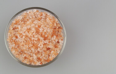Bowl with pink rock salt on gray background. Top view, copy space for text.