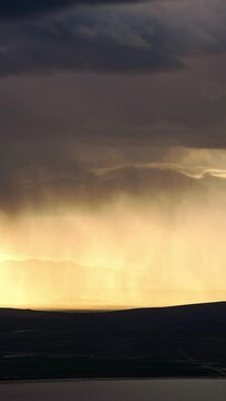 Rainstorm moving over the landscape glowing from the sun near Utah Lake during thunderstorm in Spring.