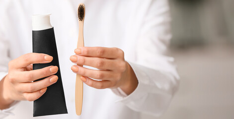 Woman with tube of activated charcoal tooth paste and bamboo brush, closeup