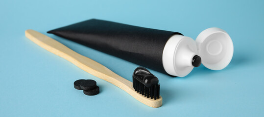 Tube of black tooth paste, brush and activated carbon pills on blue background