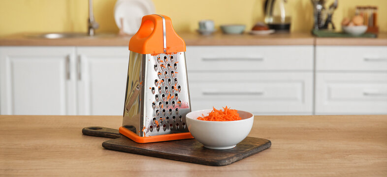 Bowl with fresh carrots and grater on kitchen table