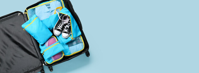 Open packed suitcase on light blue background with space for text. Travel concept