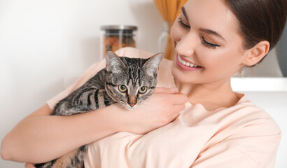Beautiful young woman with cute striped cat in kitchen