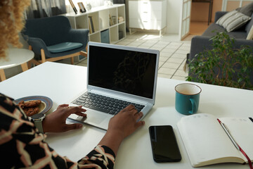 Close-up of African woman sitting at table in front of laptop and typing on keyboard doing her...