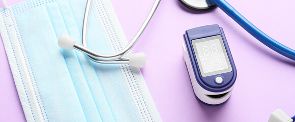 Pulse oximeter, stethoscope and medical mask on lilac background, closeup