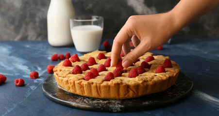 Woman decorating tasty raspberry pie on dark table