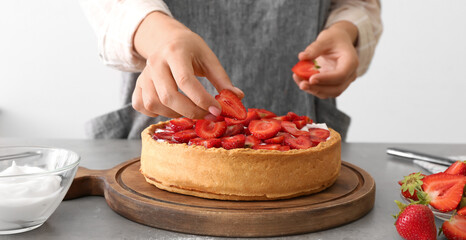 Woman decorating tasty pie with strawberry in kitchen, closeup