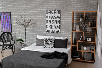 Interior of stylish bedroom with poster, glowing lights and shelving unit