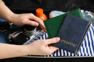 Woman holding passports near opened suitcase with traveler accessories, closeup