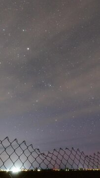 Timelapse of stars from Eastern Idaho as clouds streak through the sky looking over chainlink fence.