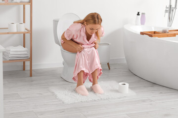 Mature woman with diarrhea sitting on toilet bowl in bathroom