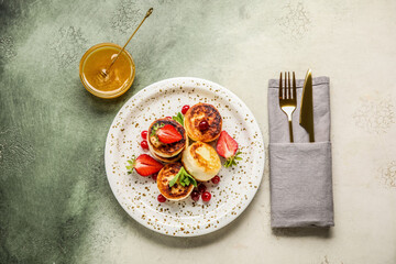 Plate with cottage cheese pancakes, cutlery and bowl with honey on grunge background