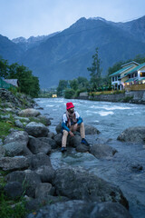 A man sitting along on the Lidder River with his shoes, Pahalgam, Jammu and Kashmir, India.