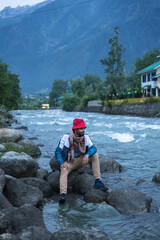 A man sitting along on the Lidder River with his shoes, Pahalgam, Jammu and Kashmir, India.