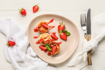 Plate with delicious cottage cheese pancakes covered with sauce and berries on white wooden background