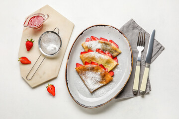 Plate of thin pancakes with strawberries, sugar powder and cutlery on white background
