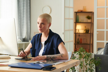 Female designer looking at monitor to retouch photos with graphic tablet while working remotely at...