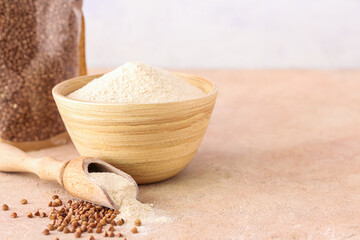 Bowl of flour and scoop with buckwheat grains on table against white background, closeup