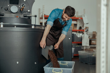 Business owner pouring roasted coffee beans into the special box from roaster machine for selling