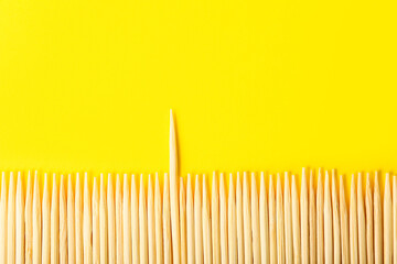 Row of wooden toothpicks on yellow background, closeup