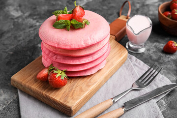 Wooden board with pink pancakes and strawberry on grunge background