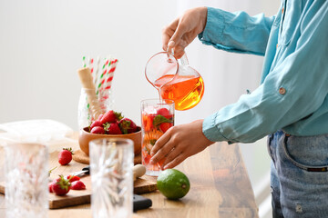 Woman preparing tasty strawberry lemonade at table in kitchen