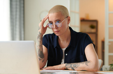 Serious woman in eyeglasses concentrating on her online work on laptop looking very exhausted...