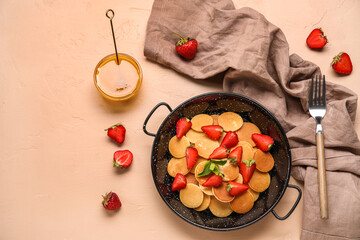 Composition with frying pan of mini pancakes, strawberry and bowl of honey on color background
